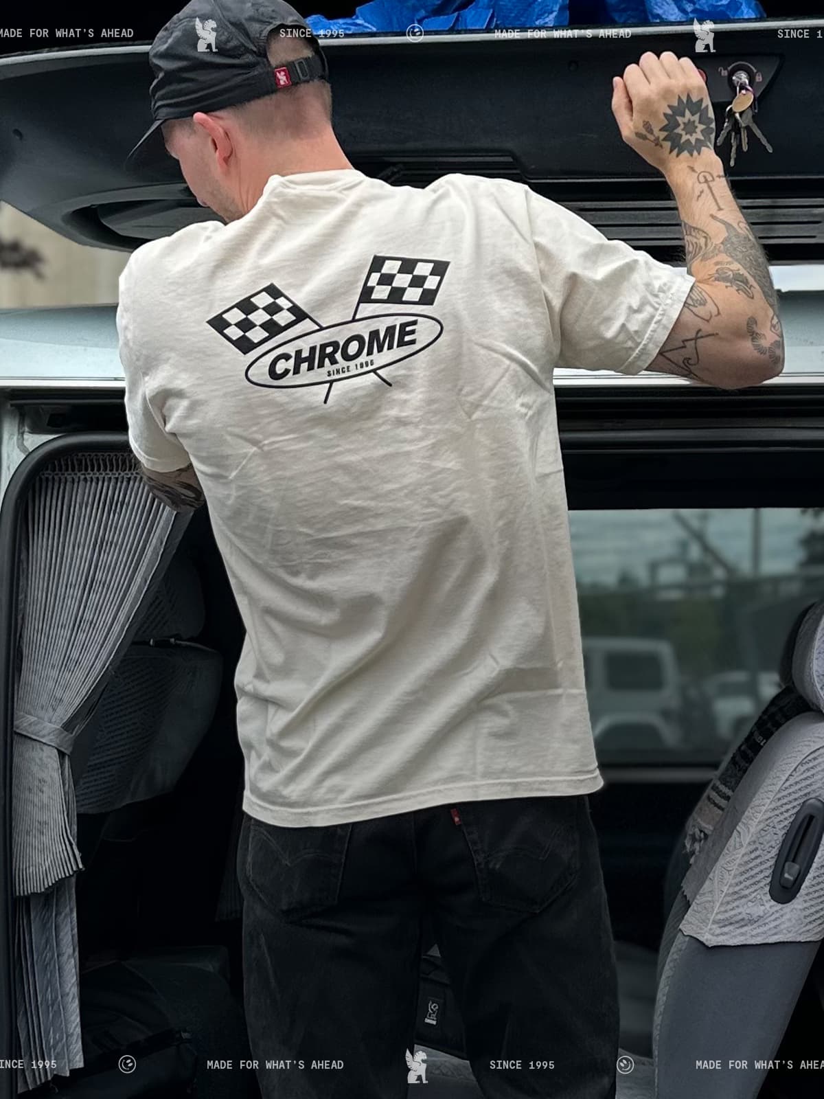 Man wearing a white t-shirt with 'Chrome' logo, standing next to an open car trunk.